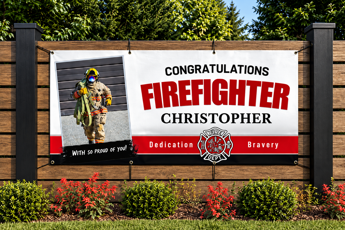 A personalized firefighter congratulations banner displayed on a wooden fence outdoors. The banner features a photo of a firefighter in full gear on the left, with the text 'CONGRATULATIONS FIREFIGHTER CHRISTOPHER' in black and red lettering on a white background.